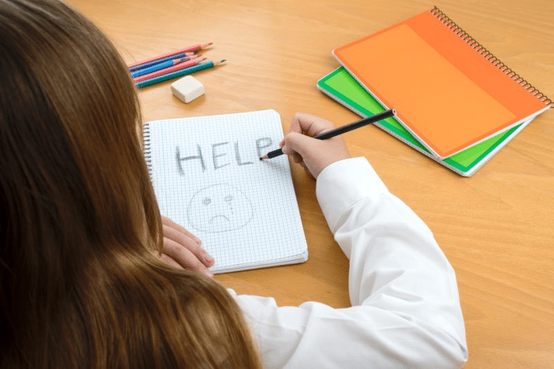 Girl drawing sad face and the word help in her notebook